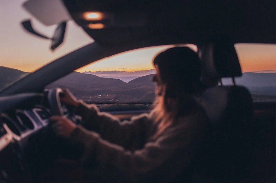 woman driving the car surrounded by beautiful scenery.