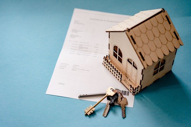 A toy wooden house and keys are placed on a sheet of paper.