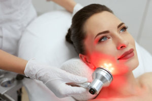 Facial Beauty Treatment. Woman Doing Red Led Light Therapy